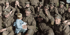 Ein Kind sitzt auf dem Schoß eines Soldaten, daneben sitzen mehrere andere Soldaten