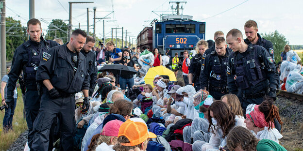 Polizisten stehen neben Aktivisten, die auf Gleisen sitzen