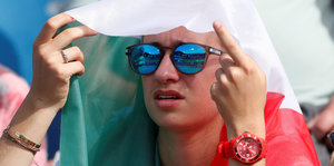 Zuschauerin mit Sonnenbrille hält sich Fahne über den Kopf