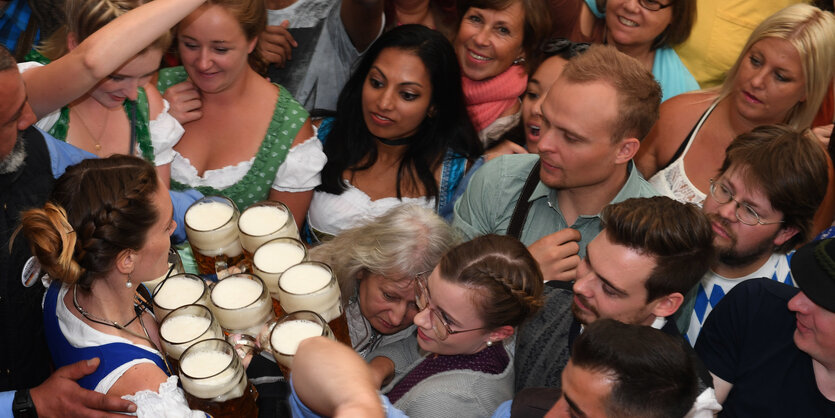 Eine Kellnern trägt zahlreiche Bierkrüge, darum sammeln sich Menschen