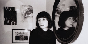 Eine Frau mit dunklem Bob steht vor einem Spiegel und schaut zur Seite