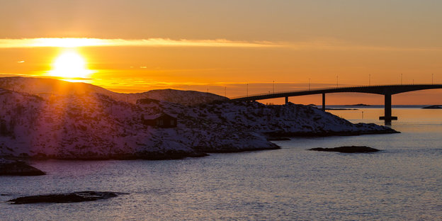 Die Sonne geht hinter der Sommaroy-Brücke unter, die die Inseln Kvaloya und Sommaroy verbindet.