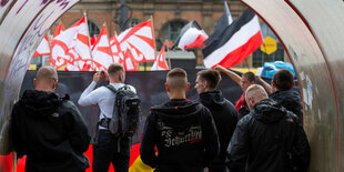 Vier Neonazis stehen mit dem Rücken zur Kamera in einer Unterführung. Sie blicken auf eine Gruppe von rechten Demonstranten