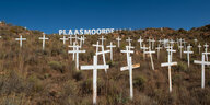 Weiße Kreuze stecken als Grabfeld in einem Hügel