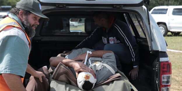 Ein Mann mit Rettungsweste schiebt eine Trage mit einem Verletzten in einen Pickup