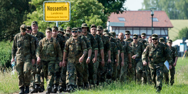 marschierende Soldaten, daneben das Ortsschild von Nossentin