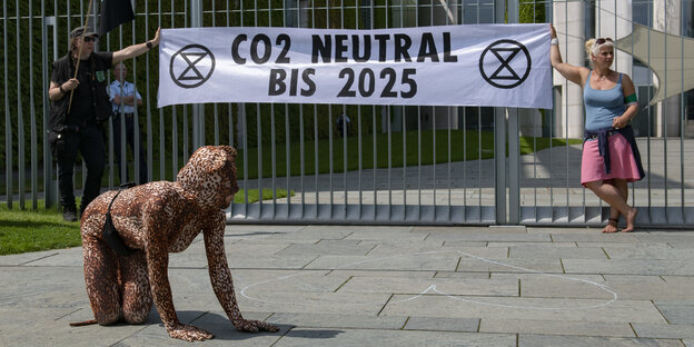 zwei Aktivisten halten ein Transparent mit der Aufschrift "CO2 Neutral bis 2025" hoch, davor kniet eine als Raubkatze verkleidete Frau