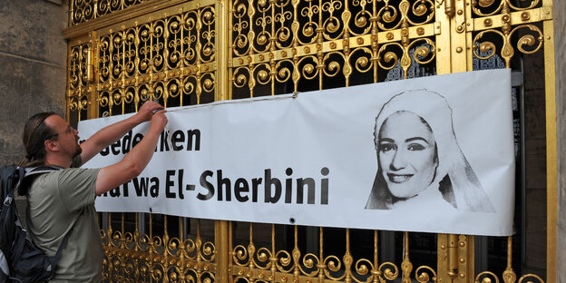 Ein Mann hängt ein Transparent auf, auf dem steht: "In Gedenken an Marwa El-Sherbini".