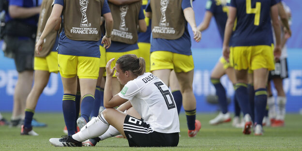Lena Oberdorf sitzt nach dem Spiel niedergeschlagen auf dem Boden, hinter ihr jubelnde Schwedinnen