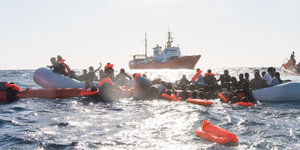 Menschen auf und an einem Schlauchboot auf Seenot. Im Hintergrund die Sea Watch