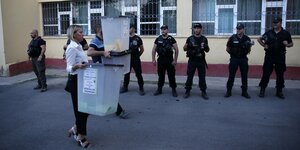 Polizisten bewachen den Auszählungsort, während eine Wahlhelferin eine Wahlurne bringt
