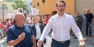 Verkehrsminister Scheuer läuft mit ausgebreiteten Armen vor demonstrierenden Menschen davon