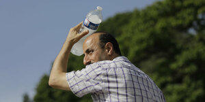 Ein Mann kühlt seinen Kopf mit einer Wasserflasche