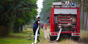 Feuerwehrmann rollt im Wald einen Löschschlauch aus.