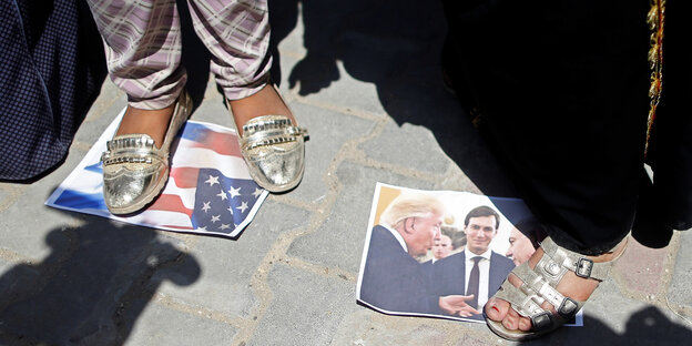Zwei Frauen stehen auf ausgedruckten Bildern von Trump und Netanjahu, die auf der Straße liegen.