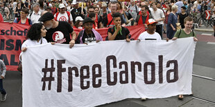 Eine Gruppe von Demonstranten hält eine Banderole, auf der "Hashtag Free Carola" steht. Sie ziehen durch eine Straße in Wien.