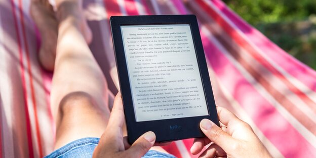 Eine Frau liegt in der Hängematte und liest auf einem E-Reader