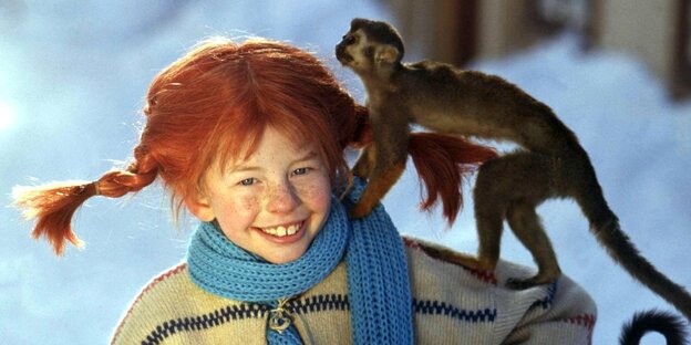Das Bild zeigt ein junges Mädchen mit einem kleinen Affen auf der linken Schulter. Das Mädchen spielt als Schauspielerin die Rolle der Pippi Langstrumpf. Es trägt rote Haare und abstehende geflochtene Zöpfe.