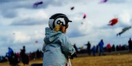 Ein Kind auf dem Tempelhofer Feld, es trägt einen Helm, hinter ihm steigen bunte Drachen