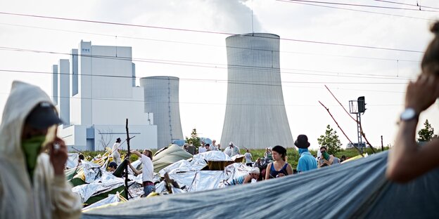 Im Vordergrund sind Demonstranten mit Zelten zu sehen, im Hintergrund rauchende Kühltürme eines Kohlekraftwerks