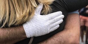 Ein Mann mit weißem Glitzerhandschuh umarmt eine Frau mit blonden Haaren