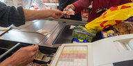 An einer Supermarktkasse in einem Lebensmittelmarkt wird mit Bargeld bezahlt.