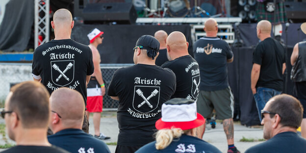 Drei Männer stehen auf dem Areal des Schild und Schwert Festivals in Sachsen mit T-Shirts der Arischen Bruderschaft.