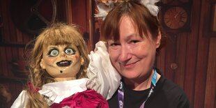 Frau posiert mit einer bezopften Horrorpuppe