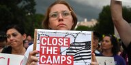 Eine Frau hält ein Plakat in der Hand auf dem "Close the camps" steht. Im Hintergrund stehen weitere Demonstranten.