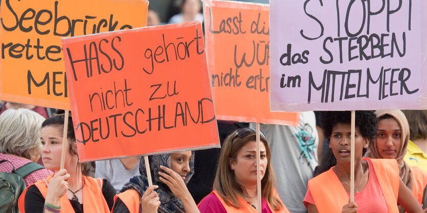 Vier Demonstrantinnen in Warnwesten halten Schilder, sie sind Teil einer Demonstration, auf einem Schild steht: Stoppt das Sterben im Mittelmeer