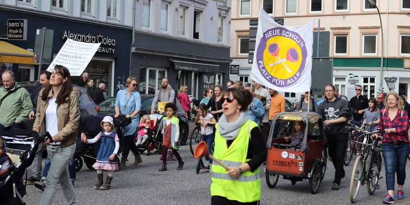 Eltern und Kinder laufen mit Protestschildern auf der Straße.