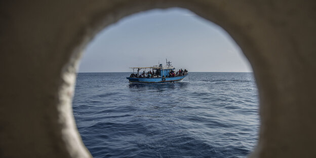 Ein Boot mit Migranten an Bord ist durch ein Bullauge des Rettungsschiffs Open Arms der spanischen Organisation Proactiva Open Arms zu sehen.