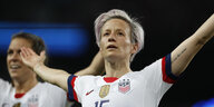 Eine Frau mit kurzen lila Haaren im Fußballtrikot breitet die Arme aus