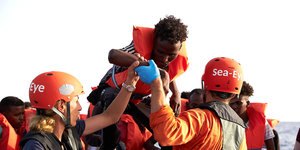 Ein Mann mit Schwimmhilfe wird von zwei NGO-Helfern an Bord eines Schiffes geholt