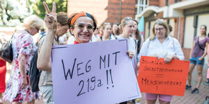 Eine Frau hält ein "Weg mit 219a" Plakat und zeigt das Victory-Zeichen