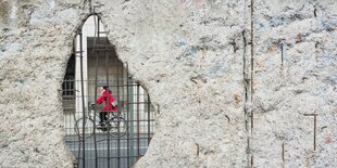 Hinter dem Loch in einer Betonmauer ist eine Radfahrerin zu sehen