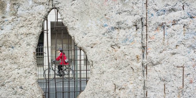 Hinter dem Loch in einer Betonmauer ist eine Radfahrerin zu sehen