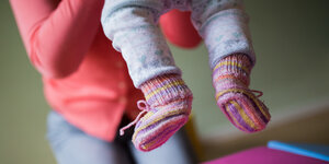 Kindertagespflege: Eine Tagespflegeperson hebt ein Kind mit selbstgestrickten Wollsocken hoch