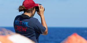 Die von der Seenotrettungsorganisation Sea-Eye herausgegebene Aufnahme zeigt ein Besatzungsmitglied des Seenotrettungsschiffes «Alan Kurdi» das mit einem Fernglas den Horizont absucht