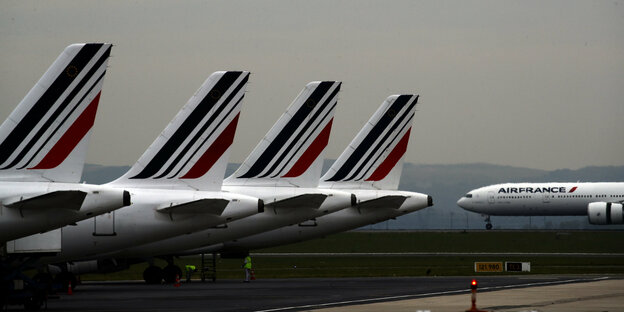 Vier Heckflügel von Air-France-Maschinen stehen auf einem Flughafen, im Hintergrund steht ein Flugzeug mit der Aufschrift Air France