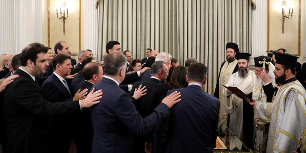 Neue griechische Minister legen den Amtseid vor Vertretern der griechisch-orthodoxen Kirche ab und fassen sich dabei gegenseitig auf die Schultern