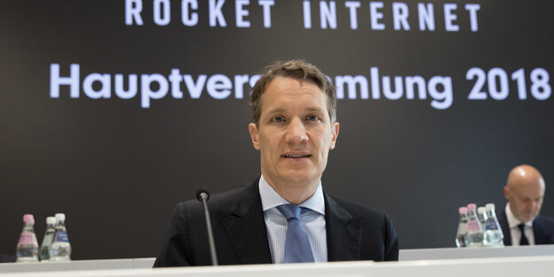 Oliver Samwer sitzt auf der Aktionärsversammlung vor einer Rocket Internet Werbewand