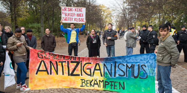 Menschen stehen hinter einem Banner mit der Aufschrift "Antiziganismus bekämpfen". Ein Mann hält ein Schildt mit der Aufschrift "Wir sind keine EU-Bürger zweiter Klasse" in die Höhe