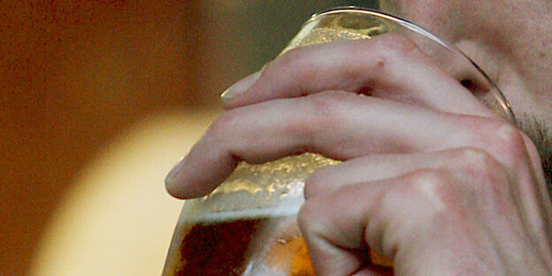 Eine Hand mit einem vollem Glas Bier wird zum Mund geführt
