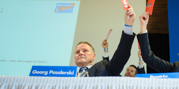 Georg Pazderski hält ene Stimmkarte in die Höhe. Im Hintergrund Thorsten Weiß