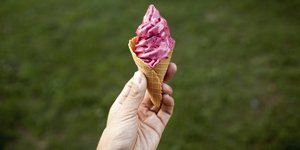 eine Hand hält eine Eiswaffel mit rosafarbener Eiscreme