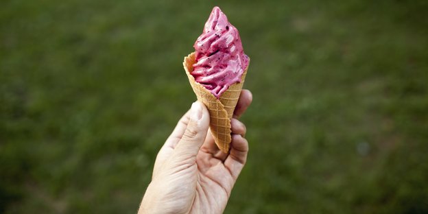 eine Hand hält eine Eiswaffel mit rosafarbener Eiscreme