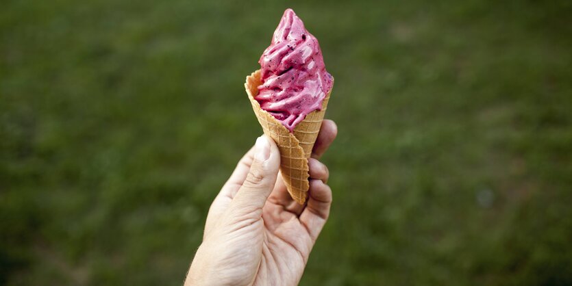 eine Hand hält eine Eiswaffel mit rosafarbener Eiscreme