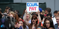 An der Parade für das Fußballteam steht eine Frau mit einem Schild, auf dem "Equal Pay" steht