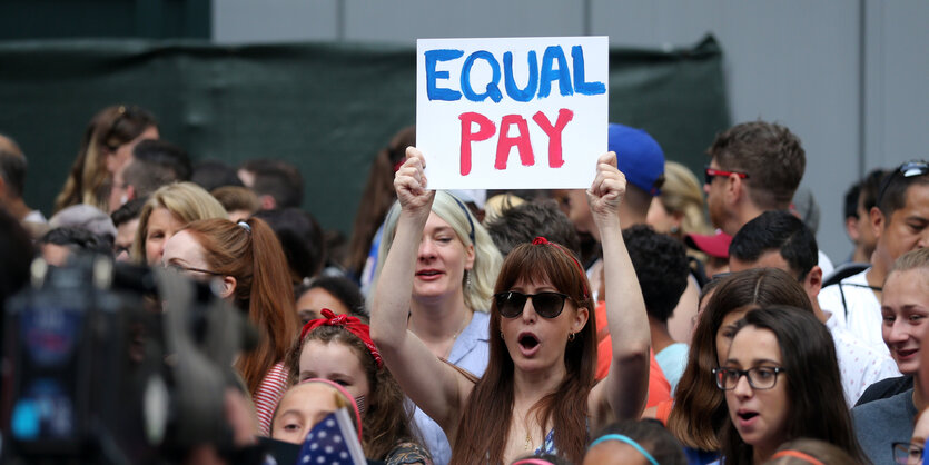 An der Parade für das Fußballteam steht eine Frau mit einem Schild, auf dem "Equal Pay" steht